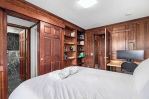 A bedroom with a bed, a desk with a computer, and built-in wooden shelving.