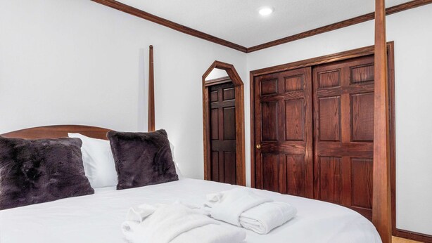 A hotel room with a bed, two pillows, a wooden wardrobe, and a door.