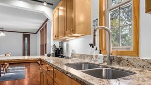 A modern kitchen with wooden cabinets, granite countertops, stainless steel sinks, and a coffee maker.