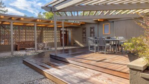 A covered outdoor patio with wooden flooring, a table and chairs, and a seating area.