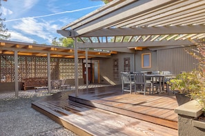 A covered outdoor patio with wooden flooring, a table and chairs, and a seating area.