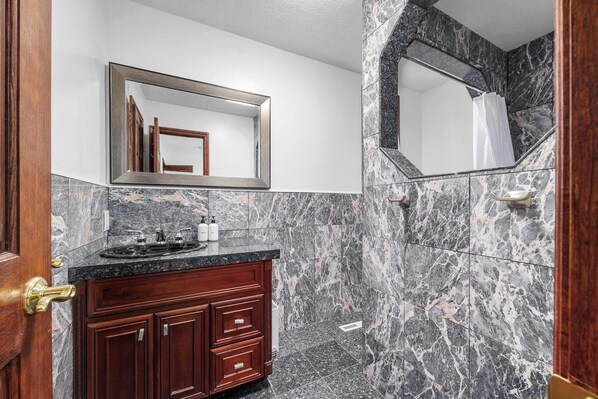 A bathroom with a marble wall, a wooden vanity, a sink, and a mirror. - Charming 3 Bedroom Home (Santa Cruz)