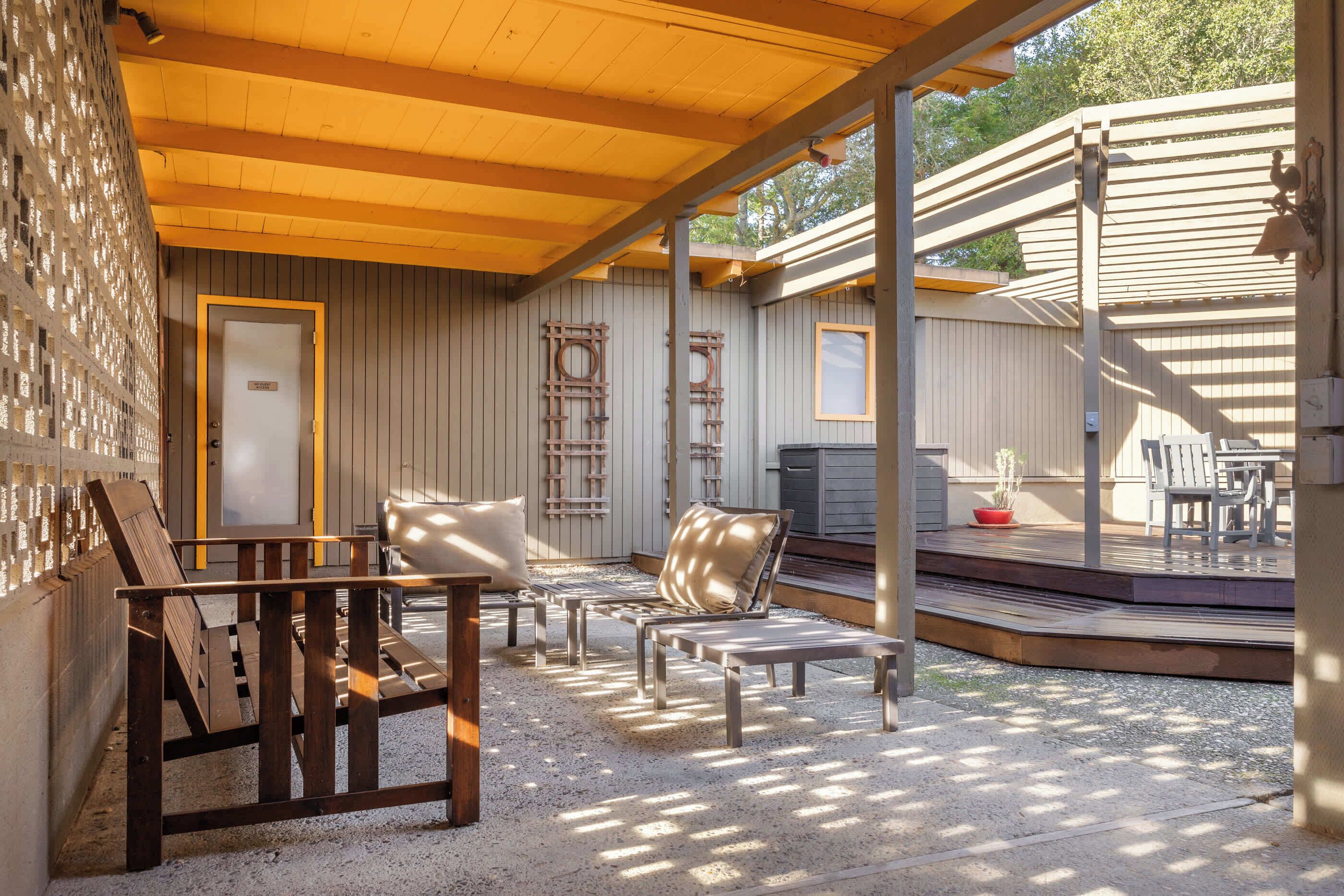 A covered outdoor seating area with wooden benches and a small table, surrounded by a wooden fence and a gravel floor.
