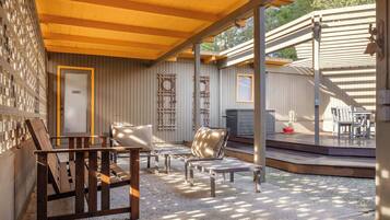A covered outdoor seating area with wooden benches and a small table, surrounded by a wooden fence and a gravel floor.