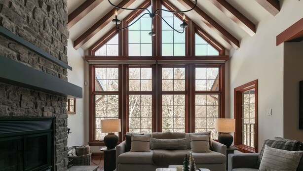A cozy living room with a stone fireplace, large windows, and a high ceiling with exposed beams. - HOT TUB - Ping-Pong - BBQ Terrace - Free Shuttle (Mont-Tremblant)