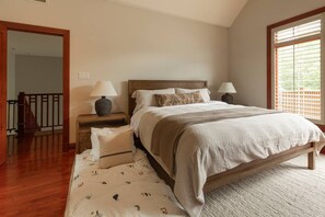 A bedroom with a bed, two bedside tables, a nightstand, a patterned rug, and a window with blinds.