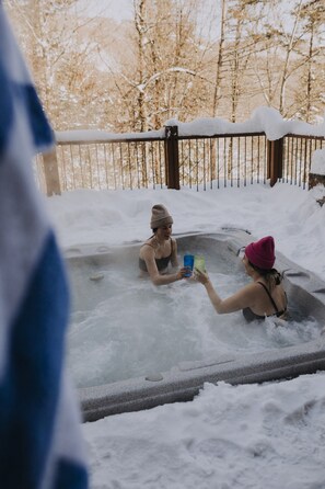 Un jacuzzi con paisajes nevados, una valla de metal y árboles al fondo.