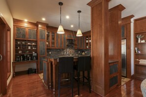 Una cocina con armarios de madera, una isla central con taburetes de bar, iluminación colgante y un refrigerador de acero inoxidable.