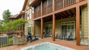 A two-story house with a covered patio area featuring a hot tub, outdoor seating, and a stone wall. - HOT TUB - Ping-Pong - BBQ Terrace - Free Shuttle (Mont-Tremblant)