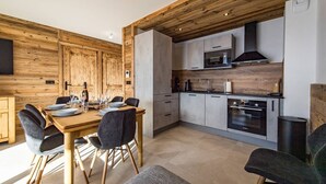 Une cuisine moderne agrémentée d’éléments en bois, un coin repas avec une table et des chaises en bois, et des appareils électroménagers intégrés.