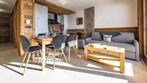 Un salon moderne avec une table et des chaises de salle à manger en bois, un canapé gris et un mur d’accent en pierre.