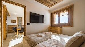Une chambre à coucher avec un lit, un téléviseur fixé au mur, un bureau en bois et une fenêtre donnant sur un beau paysage.