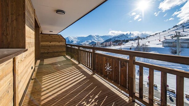 Un balcon en bois offrant une vue sur un paysage montagneux enneigé.