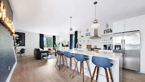 A modern kitchen with a central island, bar stools, stainless steel appliances, and a dining area with a sofa and chairs.