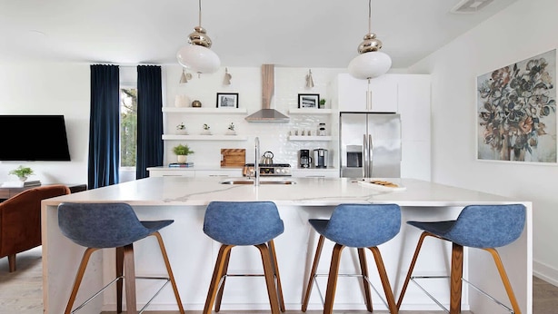 A modern kitchen with a central island, bar stools, a flat-screen TV, and a painting on the wall.