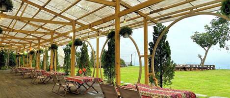 Un patio cubierto al aire libre con suelo de madera, mesas con manteles rojos y sillas.