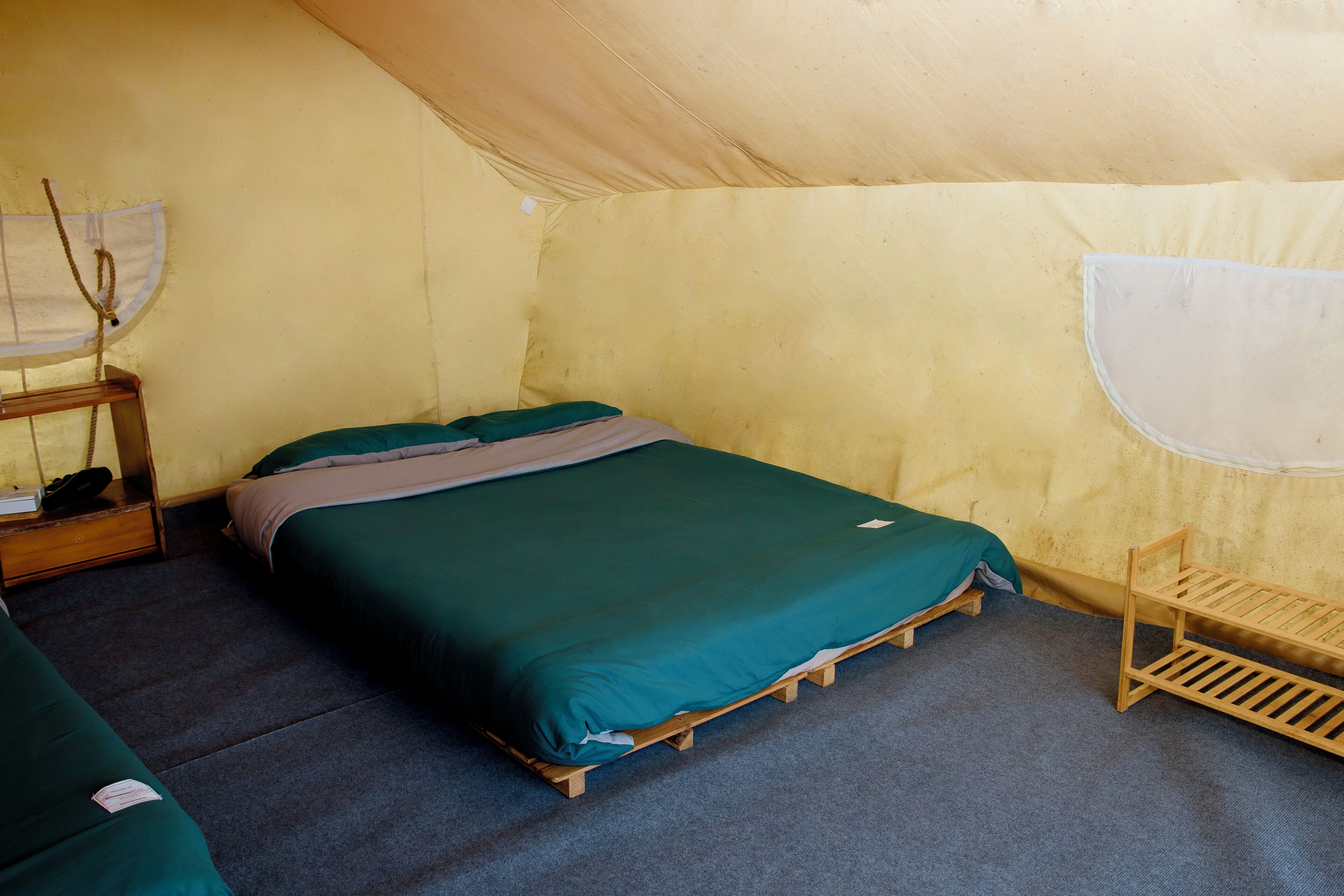 A tent with a single bed, a small wooden shelf, and a bench.