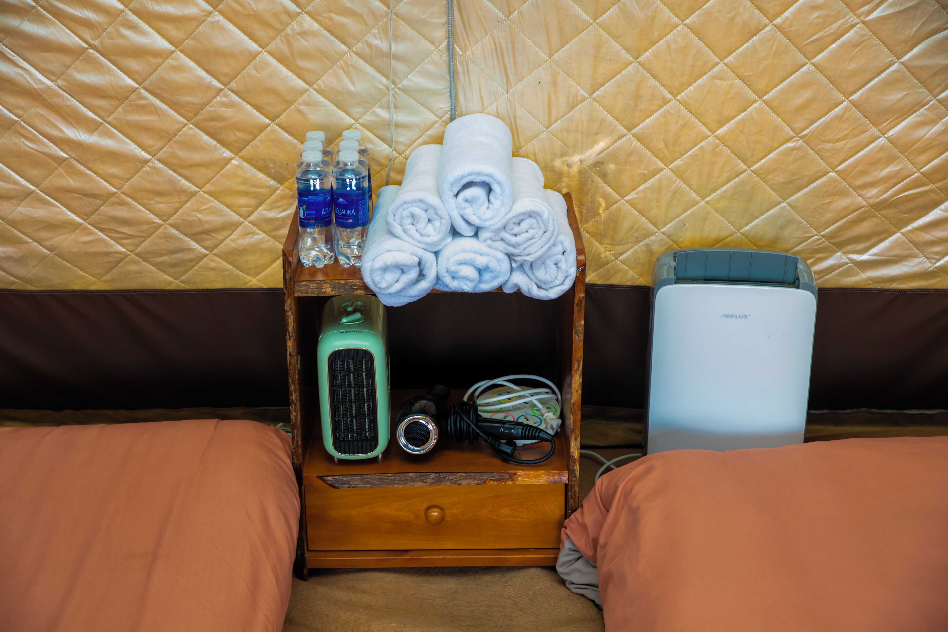 A wooden bedside table with toiletries, a hairdryer, and a portable heater.