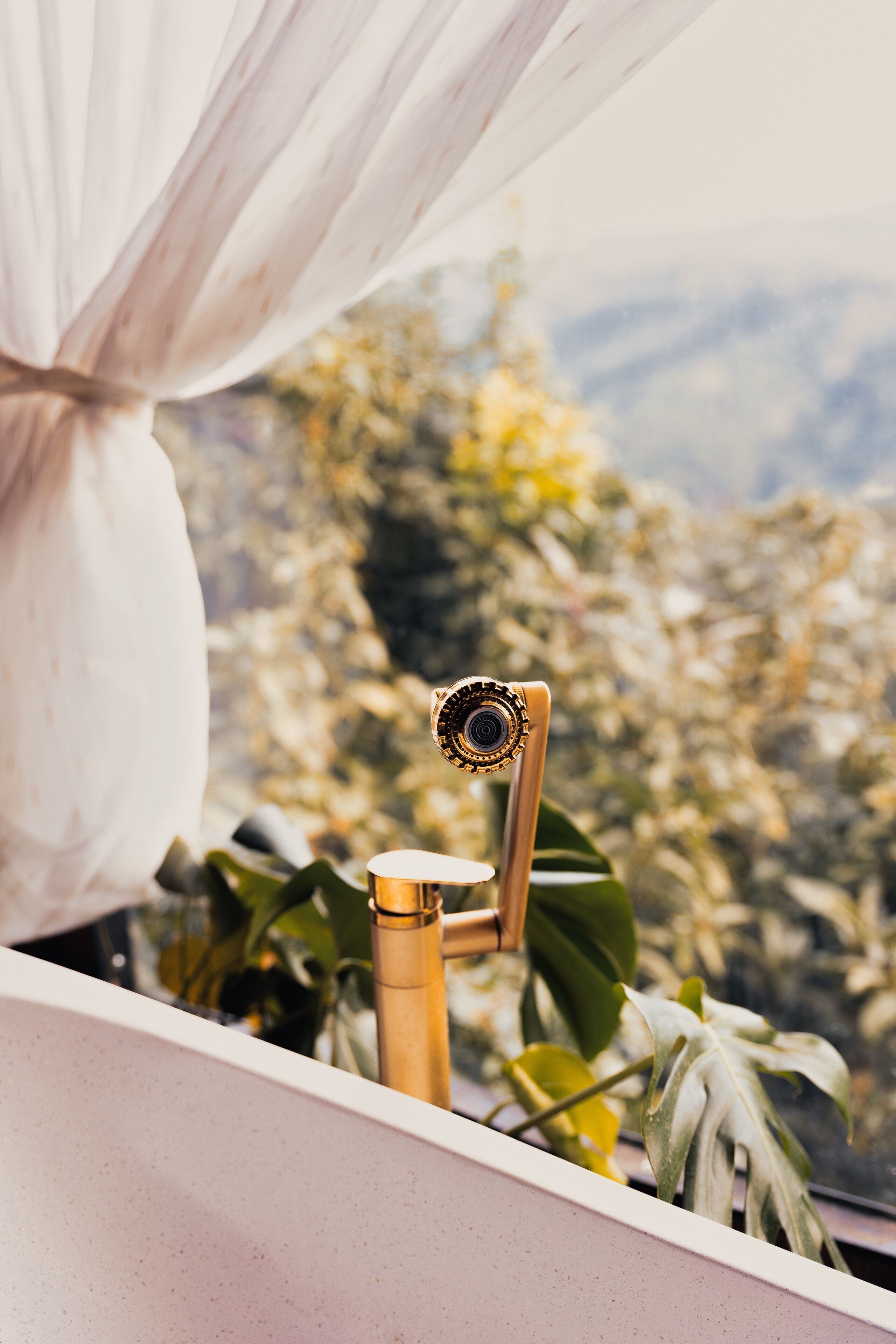 A bathroom with a gold faucet, white sink, and a view of a mountainous landscape through a window.
