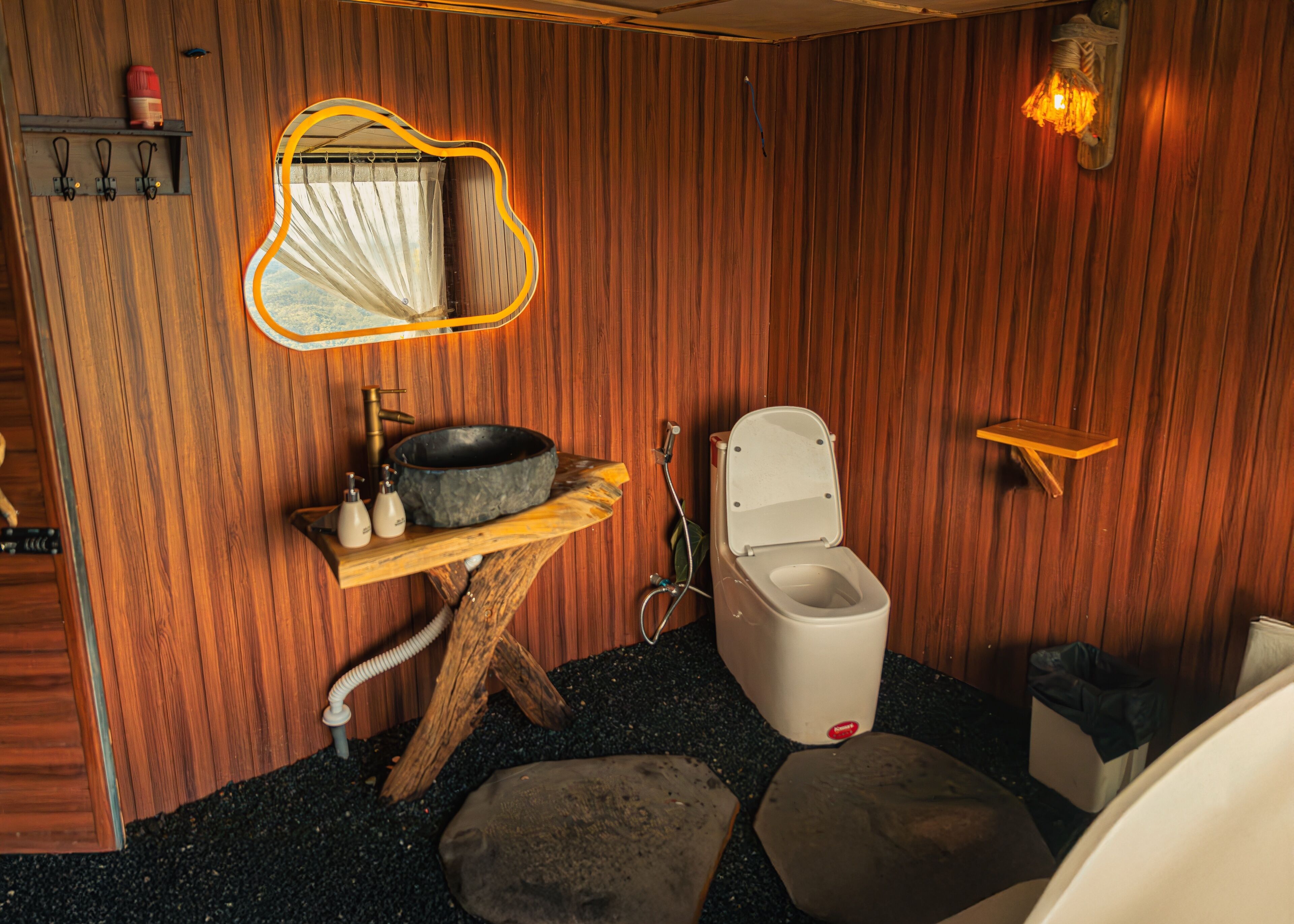 A wooden bathroom with a rustic design, including a wooden sink, a toilet, and a mirror with a unique shape.