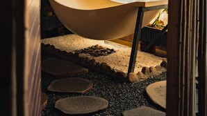 Un bagno moderno con una vasca da bagno indipendente, elementi in legno e un vialetto di ciottoli che conduce alla vasca.