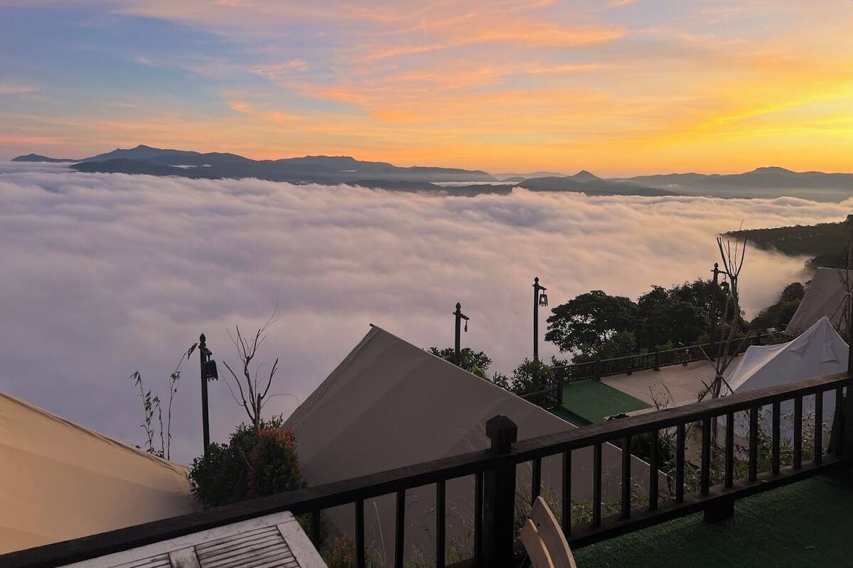 A view from a balcony overlooking a valley with a blanket of clouds below and a sunset in the distance.