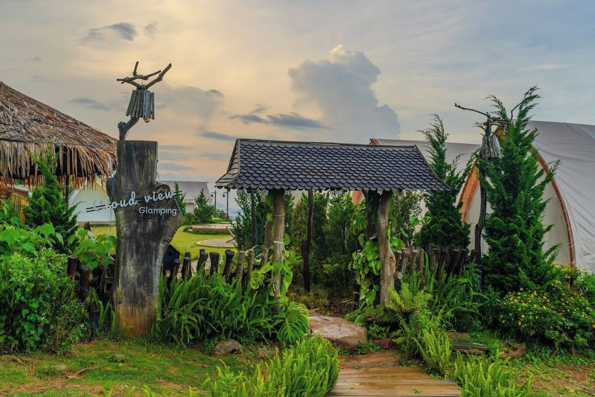 A rustic campsite with a thatched-roof hut, a small gazebo, and a tent.