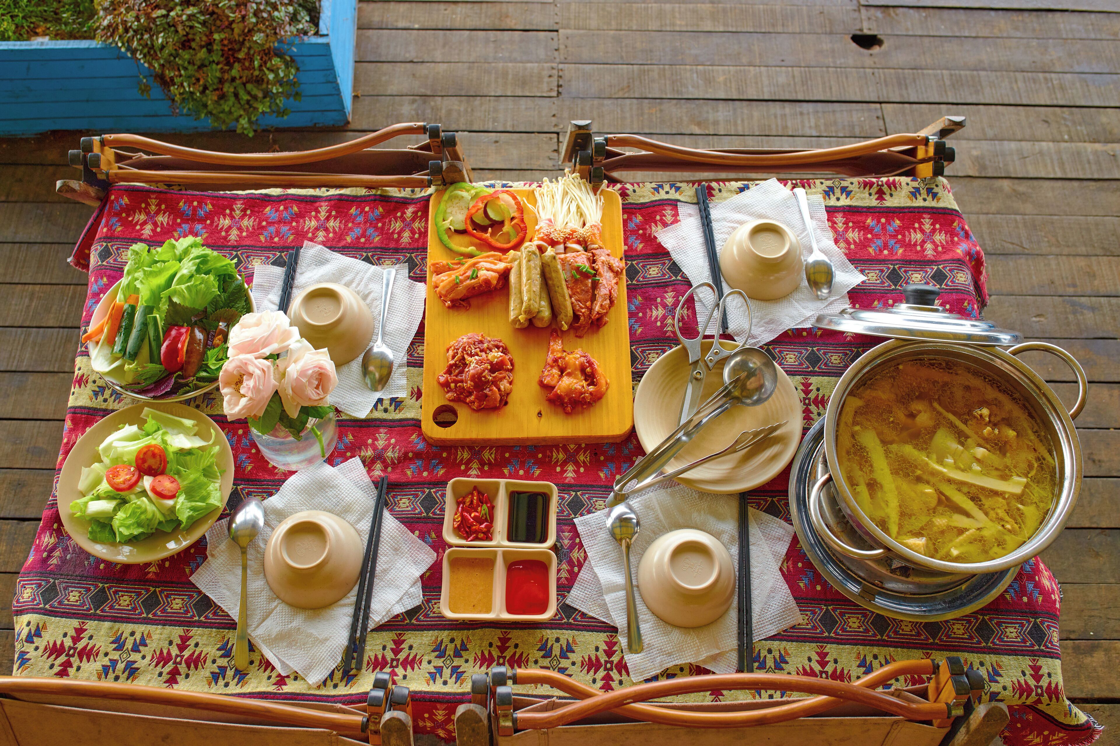 A table set with various dishes, including a salad, pickles, and a pot of soup, on a patterned tablecloth.