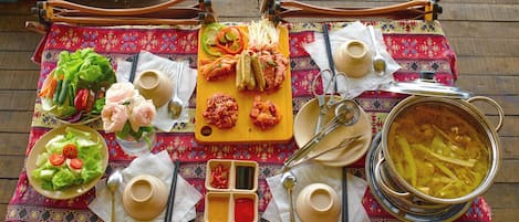 A table set with various dishes, including a salad, pickles, and a pot of soup, on a patterned tablecloth.