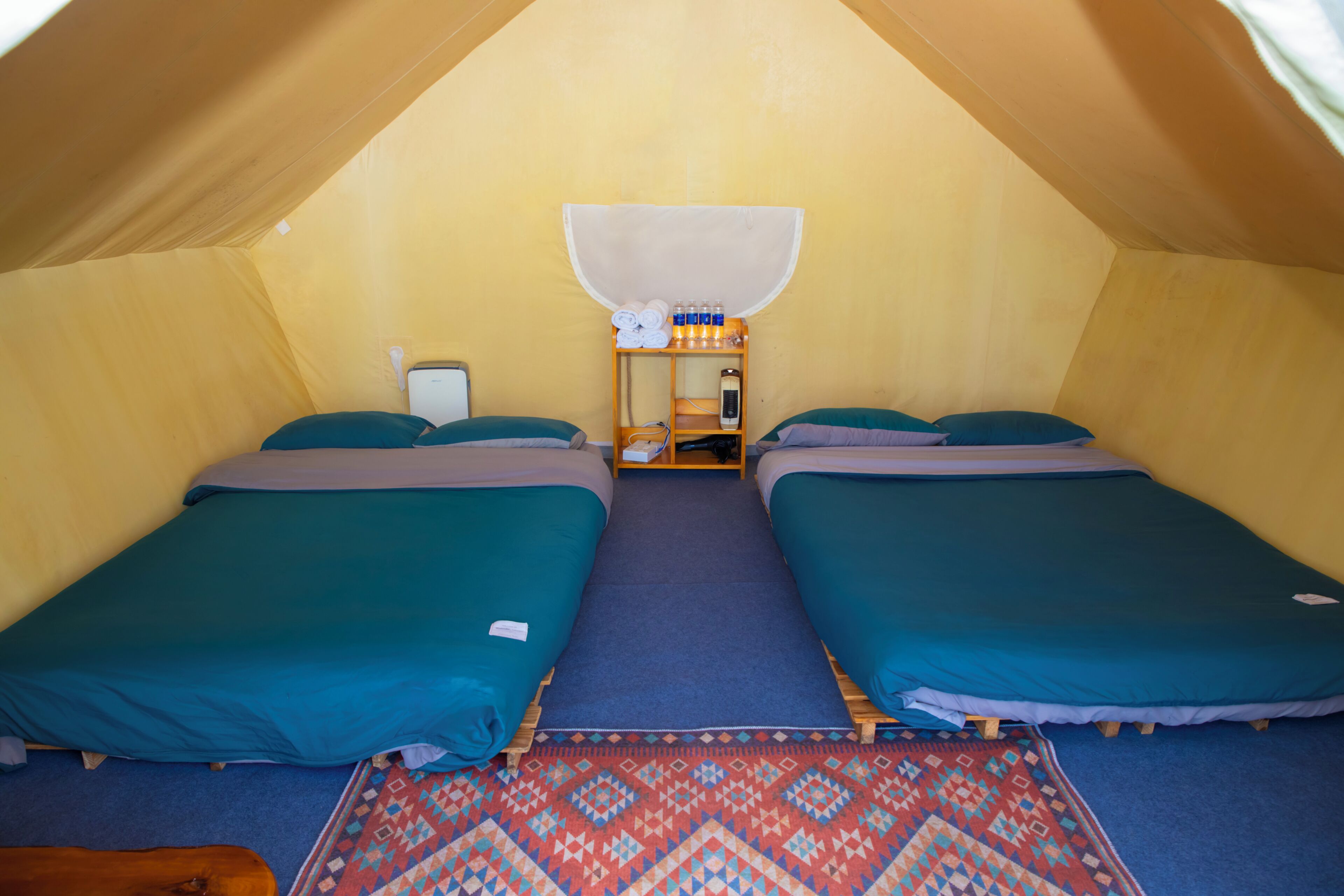 Una habitación con carpa que tiene dos camas, una mesita con artículos de aseo personal y un tapete estampado.