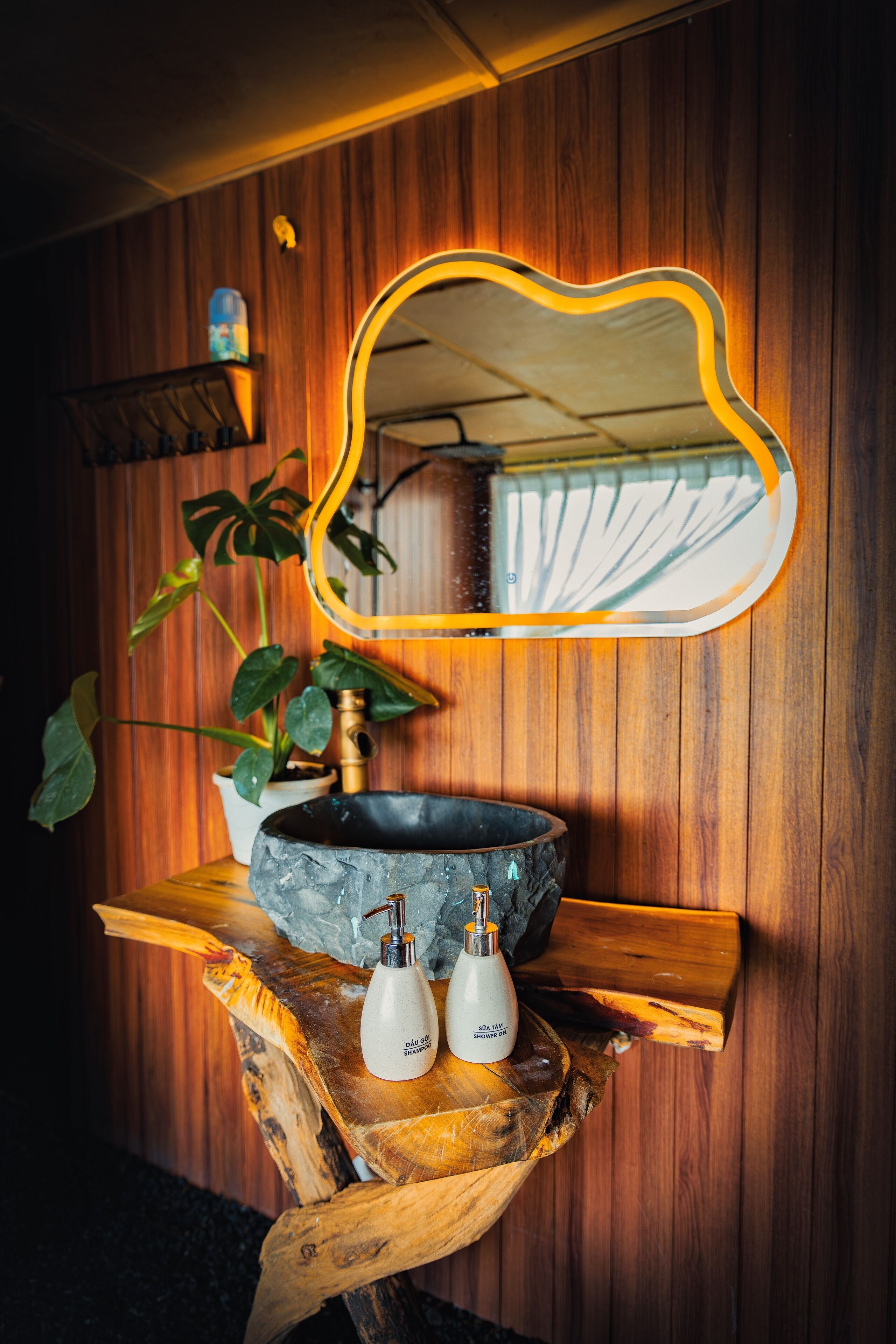 Un tocador de baño con fondo de madera, un espejo redondo con marco amarillo, un lavabo de mármol y dos botellas blancas sobre una bandeja de madera.