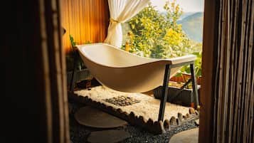 A freestanding bathtub in a room with a view of greenery and mountains.