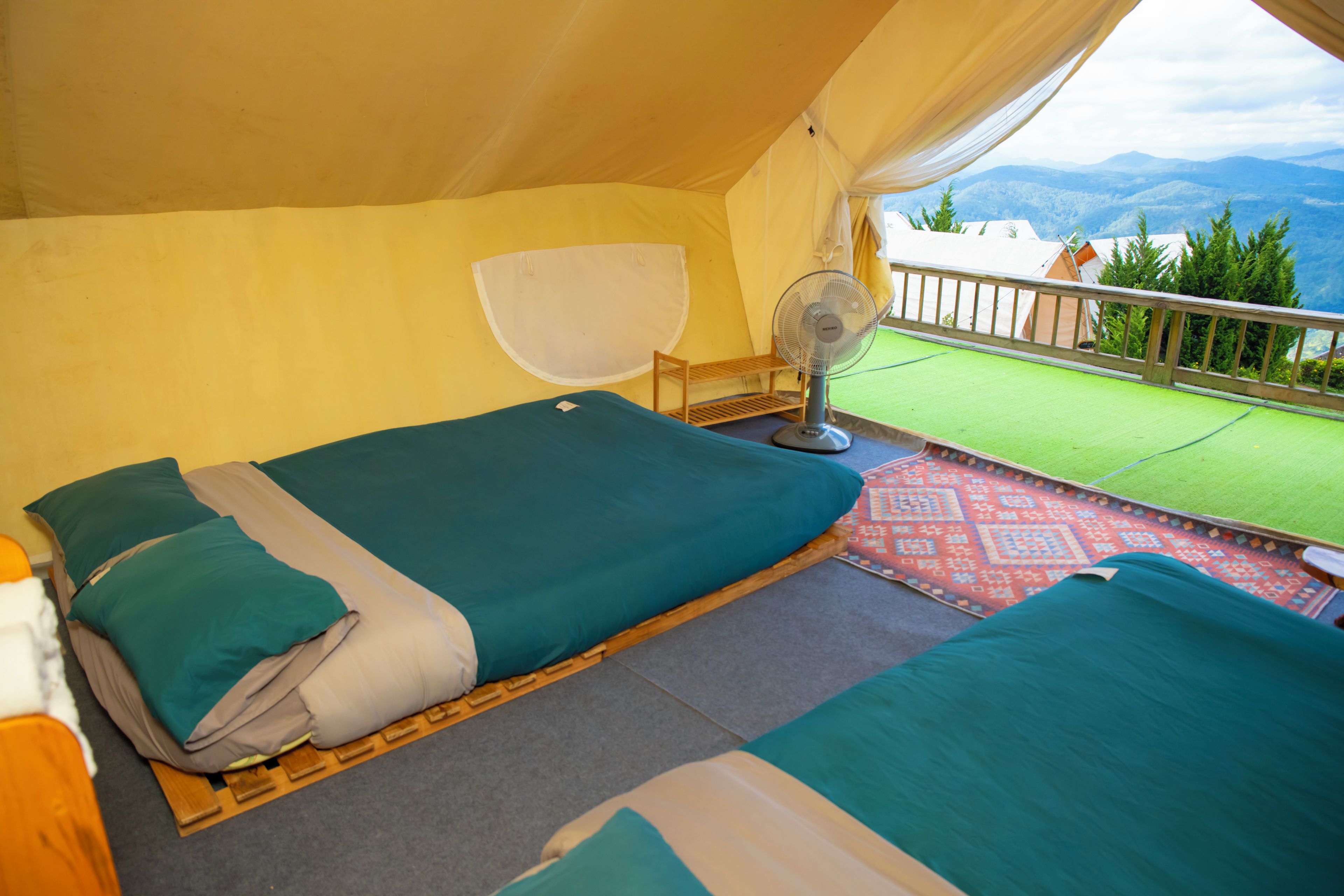 A tented accommodation with two beds, a fan, and a view of the mountains.