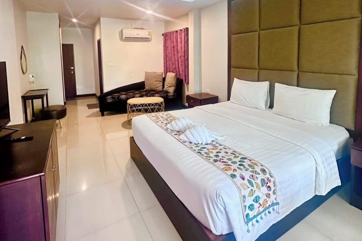 A modern hotel room with a large bed, a desk, a sofa, and an air conditioning unit.