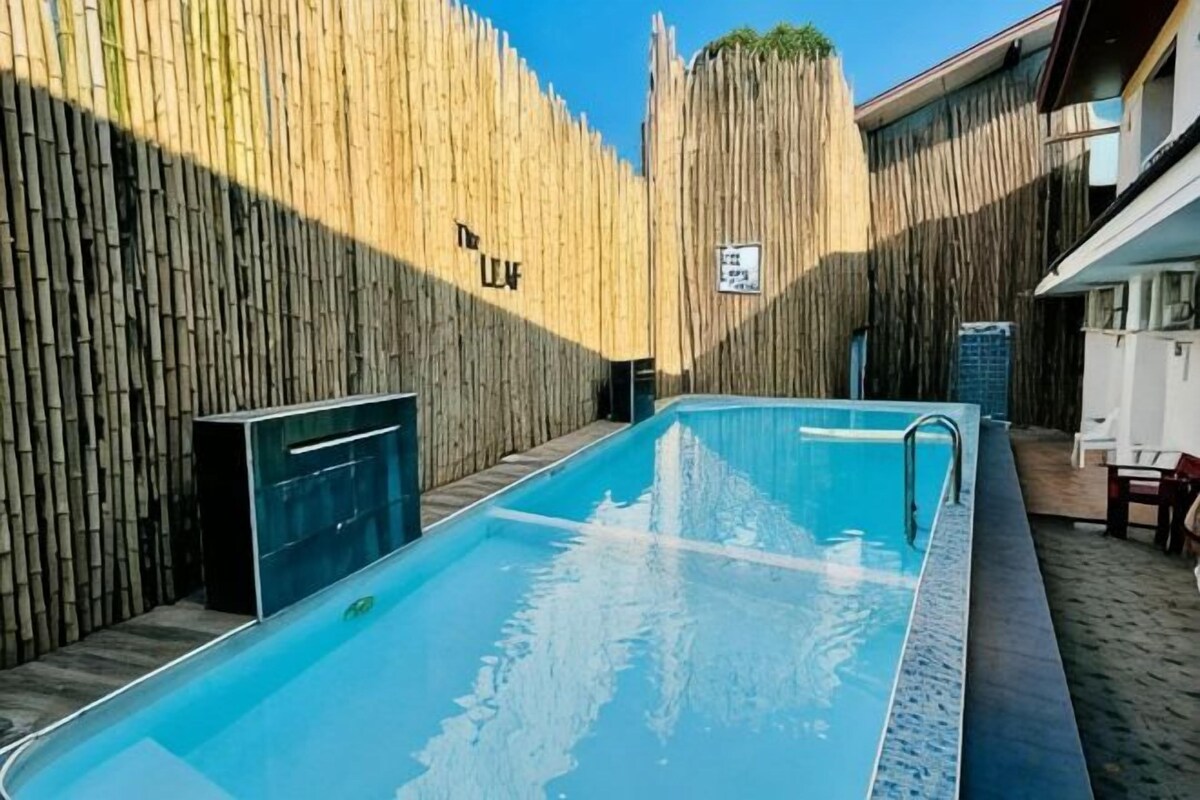 A swimming pool with a wooden fence, a sign with 'The Leaf' text, and a small outdoor seating area.