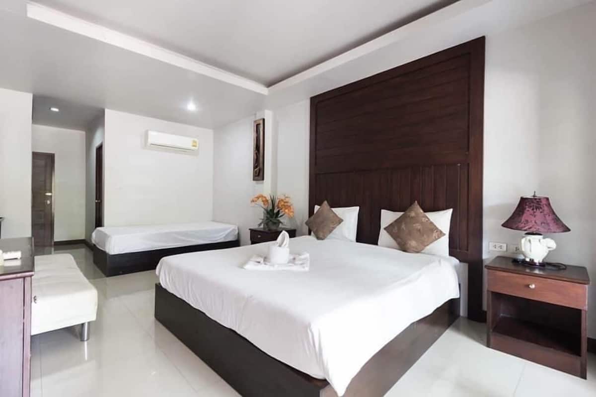 A hotel room with two beds, a wooden headboard, a nightstand with a lamp, and a small table with a vase of flowers.
