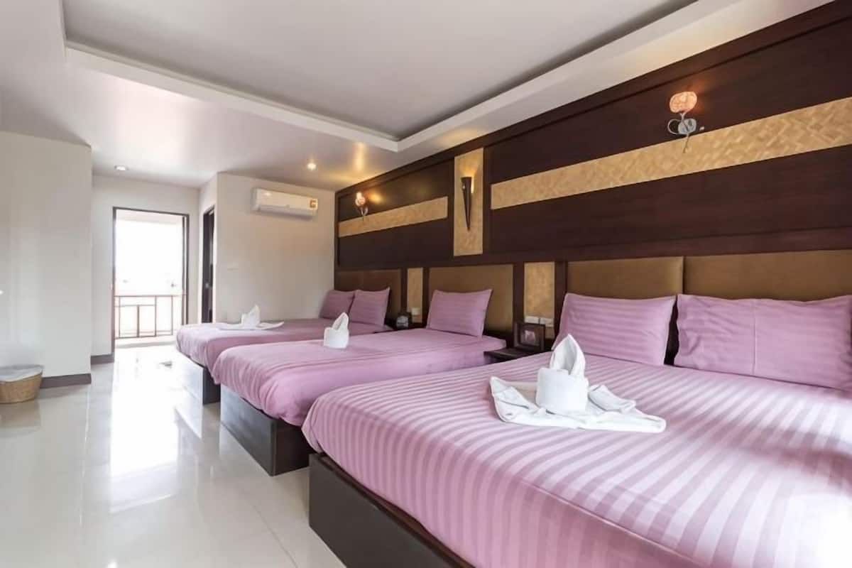 A hotel room with three beds, a wooden headboard, and a view of the outdoors.