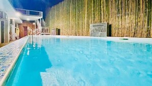 An indoor swimming pool with clear water, a wooden fence, and a building with a balcony in the background. - The leaf&pool hostel (Koh Lan)