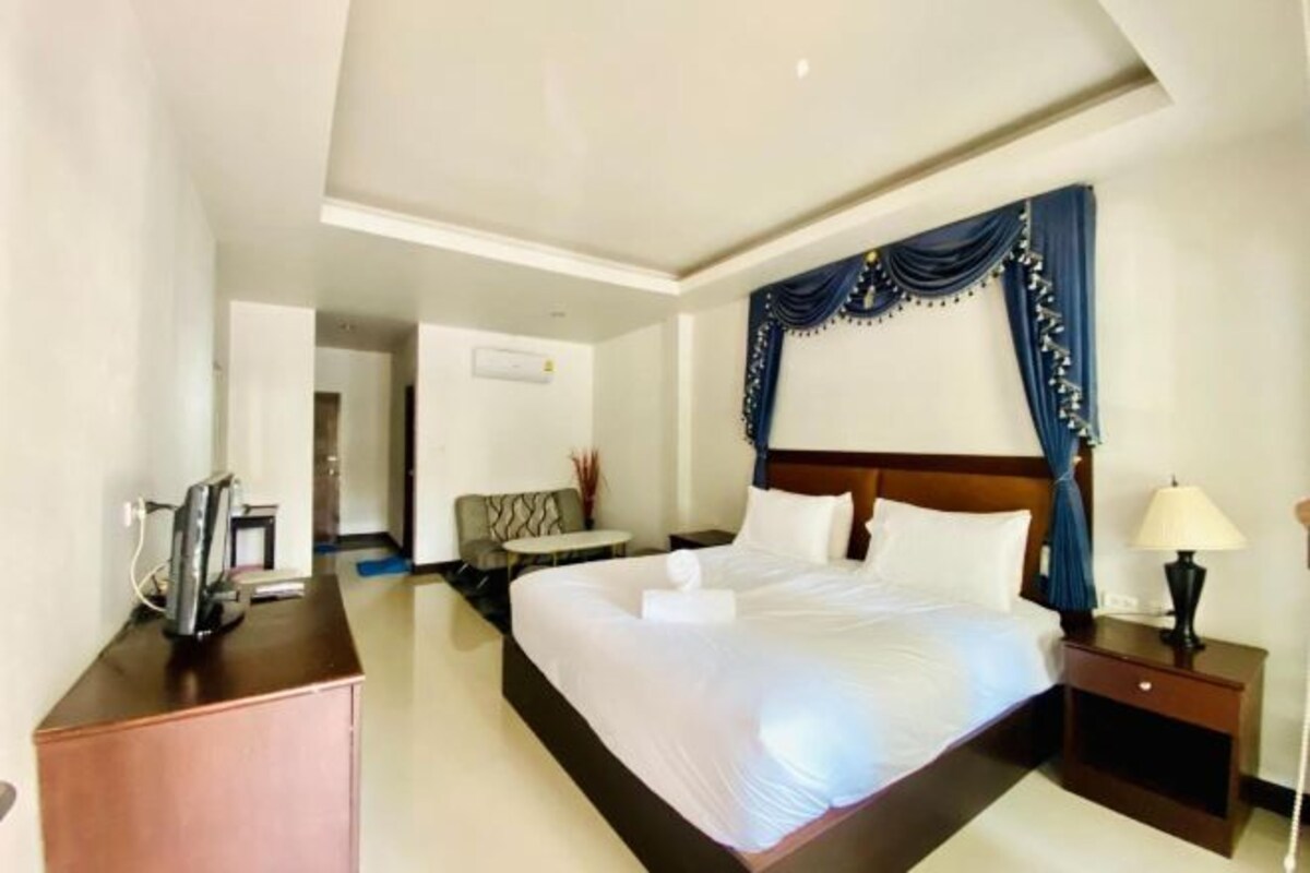 A hotel room with a large bed, a desk with a computer, a small table, and a chair.