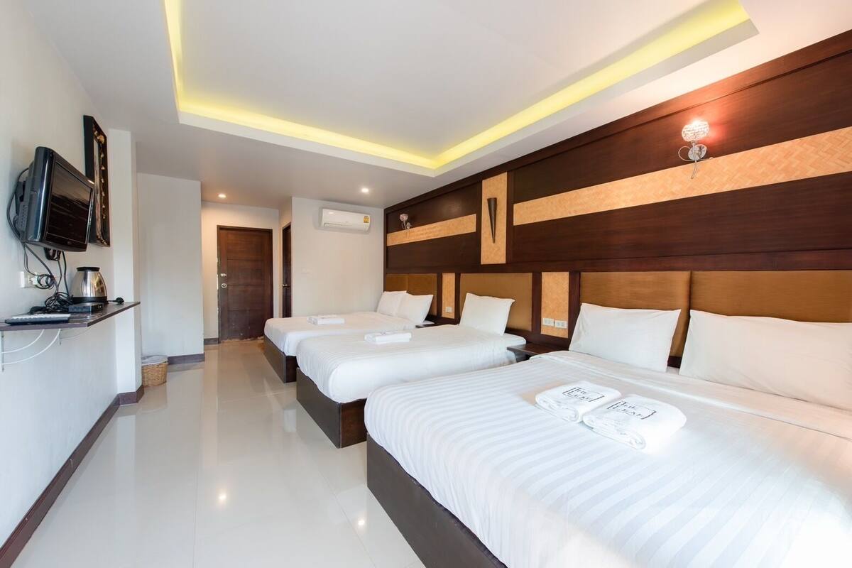A hotel room with three beds, a TV, a coffee machine, and a flat-screen TV mounted on the wall.