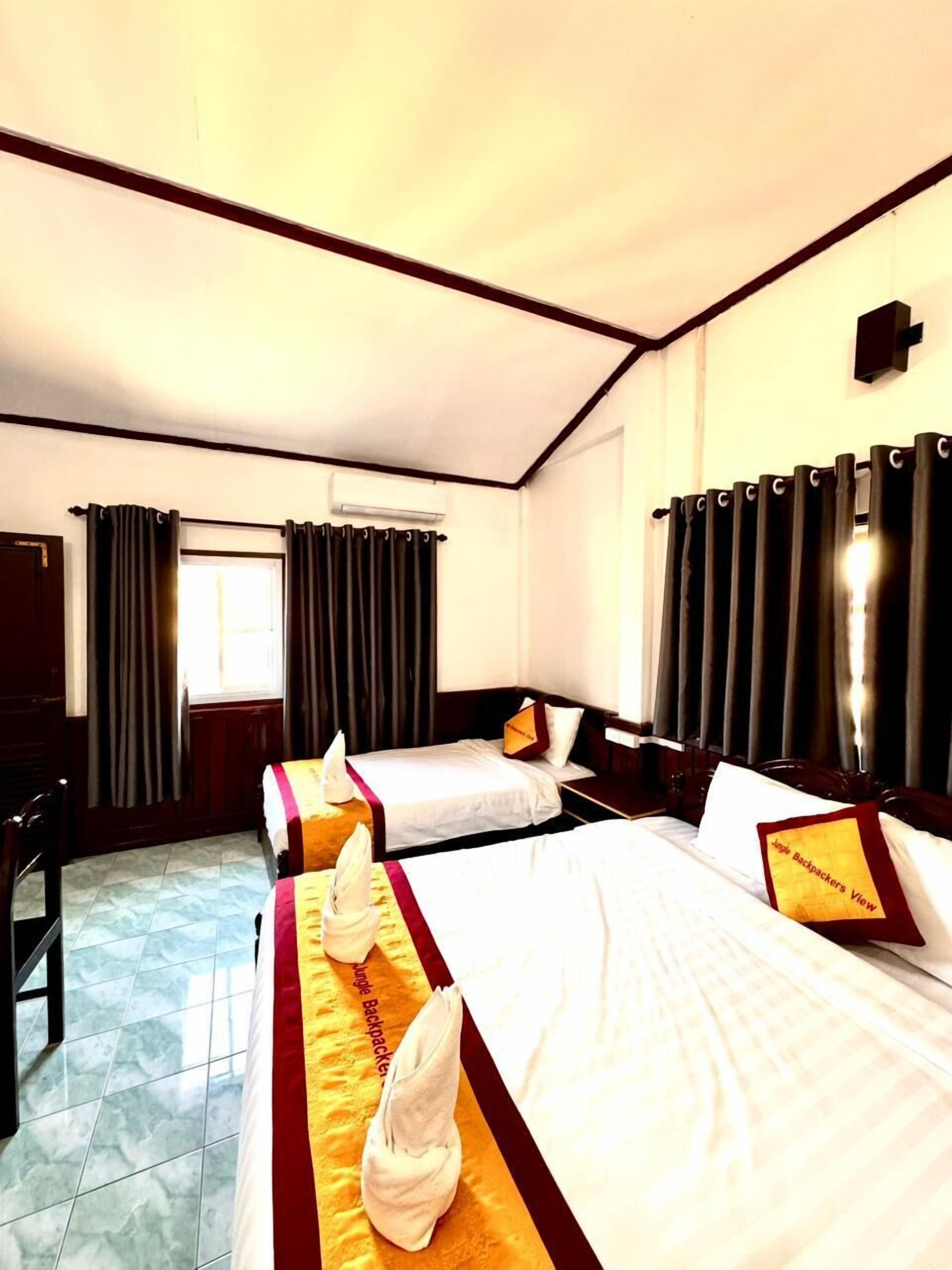 A hotel room with two beds, a desk, and a window with curtains.