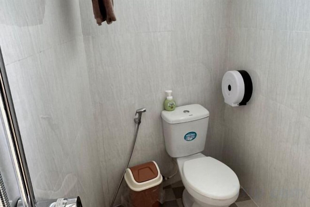 A bathroom with a toilet, a hand dryer, and a trash bin.