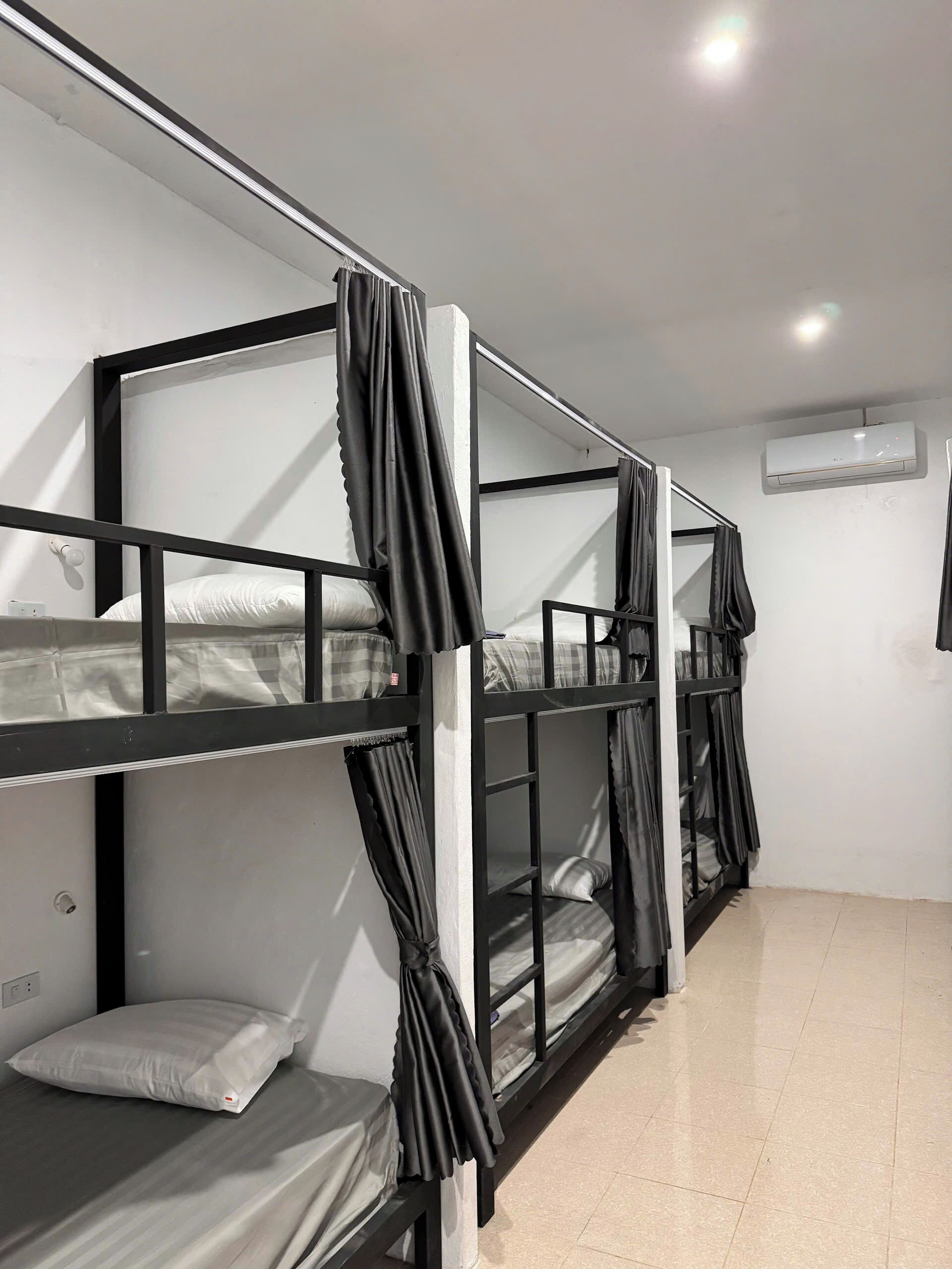 Une chambre de dortoir avec des lits superposés, un climatiseur blanc et un sol carrelé.