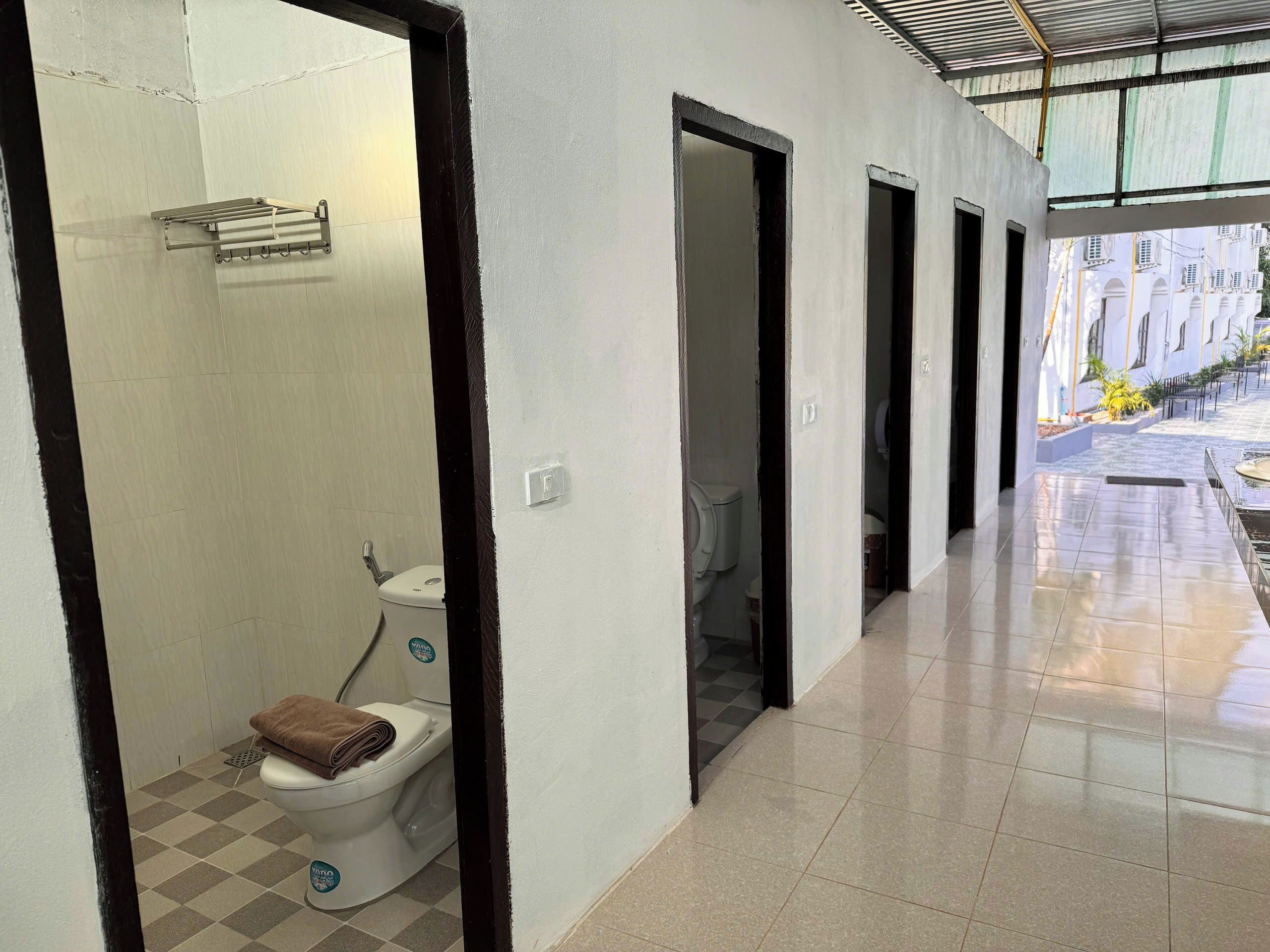A corridor with a tiled floor leading to a bathroom with a toilet and a towel.