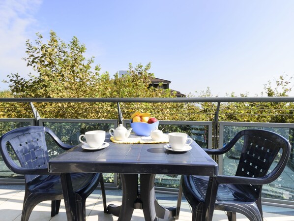 Een balkon met een tafeltje gedekt voor twee personen, met een fruitschaal, twee kopjes en een theepot.