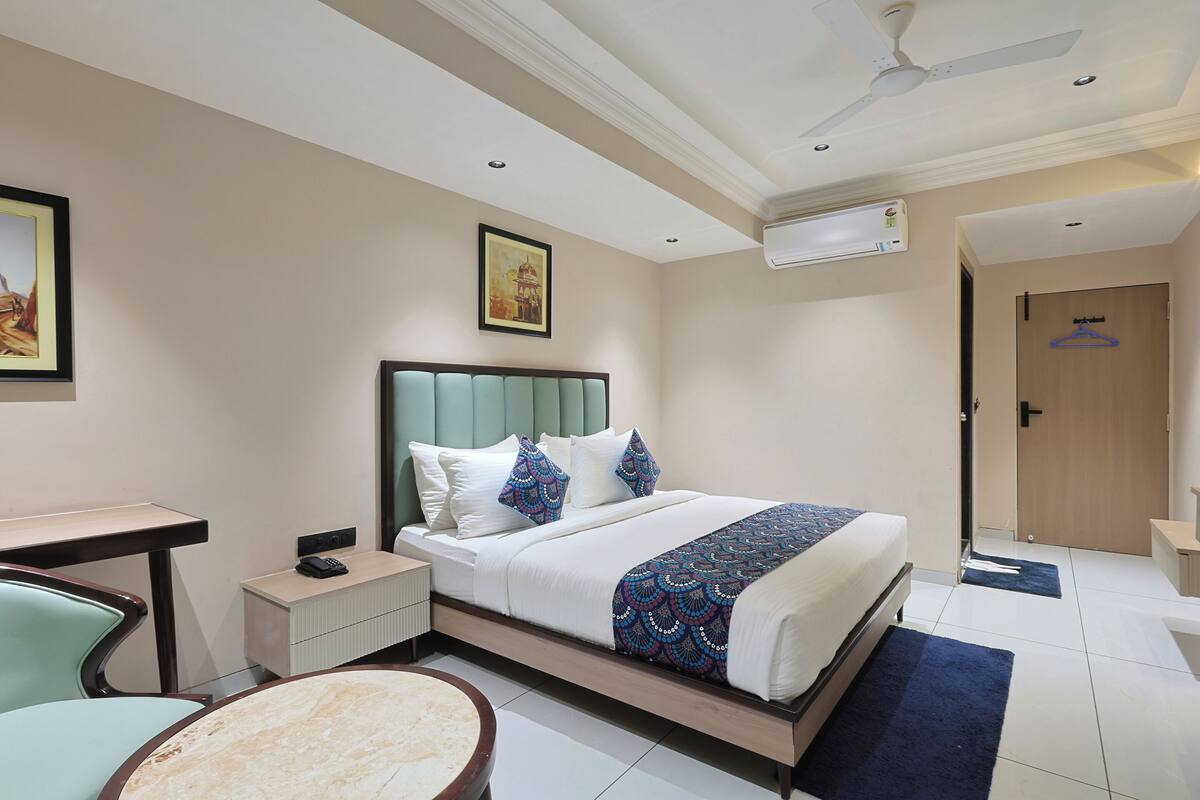 Una habitación de hotel con una cama, mesita de noche, silla y escritorio.