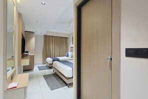 Una habitación de hotel con dos camas, un escritorio, un espejo, un armario y un ventilador de techo.