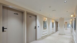Ein Hotelgang mit den Nummern 207 und 208, Bilderrahmen an den Wänden und eingelassener Beleuchtung.