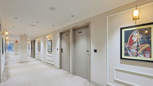 Ein Hotelgang mit Türen, auf denen 211 und 212 stehen, Leuchten und einem gerahmten Kunstwerk an der Wand.