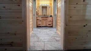 Un couloir intérieur en bois mène à une salle de bain équipée d’un meuble-lavabo et d’un miroir.